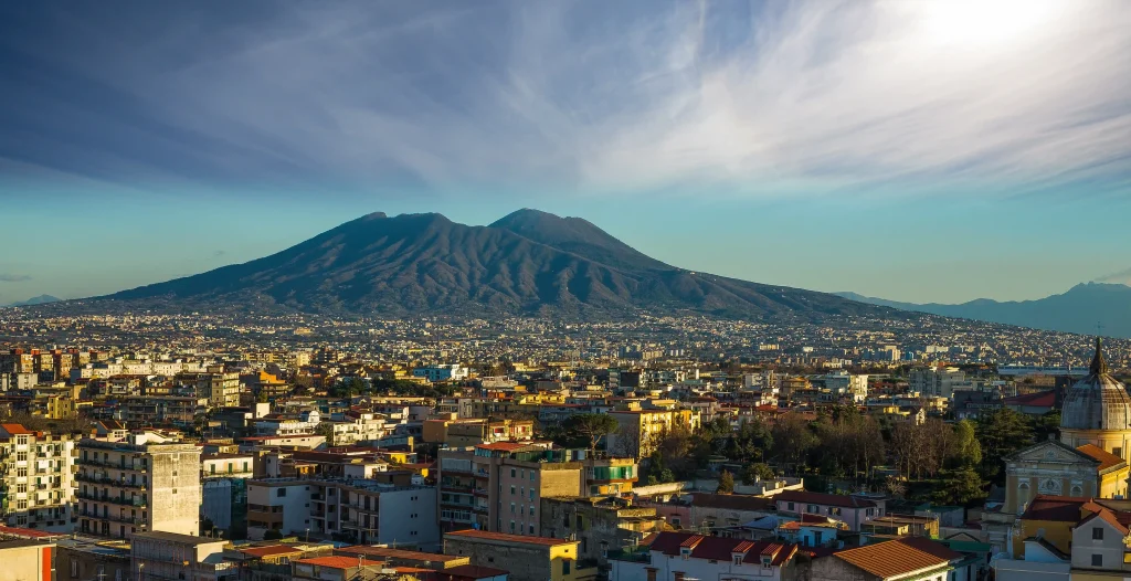 Hidden panoramic view of Naples featuring ancient rooftops, narrow historic streets, Mount Vesuvius, and the Bay of Naples at sunset, representing the hidden side of Naples and its secret gems.