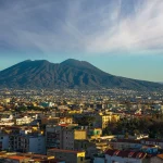 Hidden panoramic view of Naples featuring ancient rooftops, narrow historic streets, Mount Vesuvius, and the Bay of Naples at sunset, representing the hidden side of Naples and its secret gems.