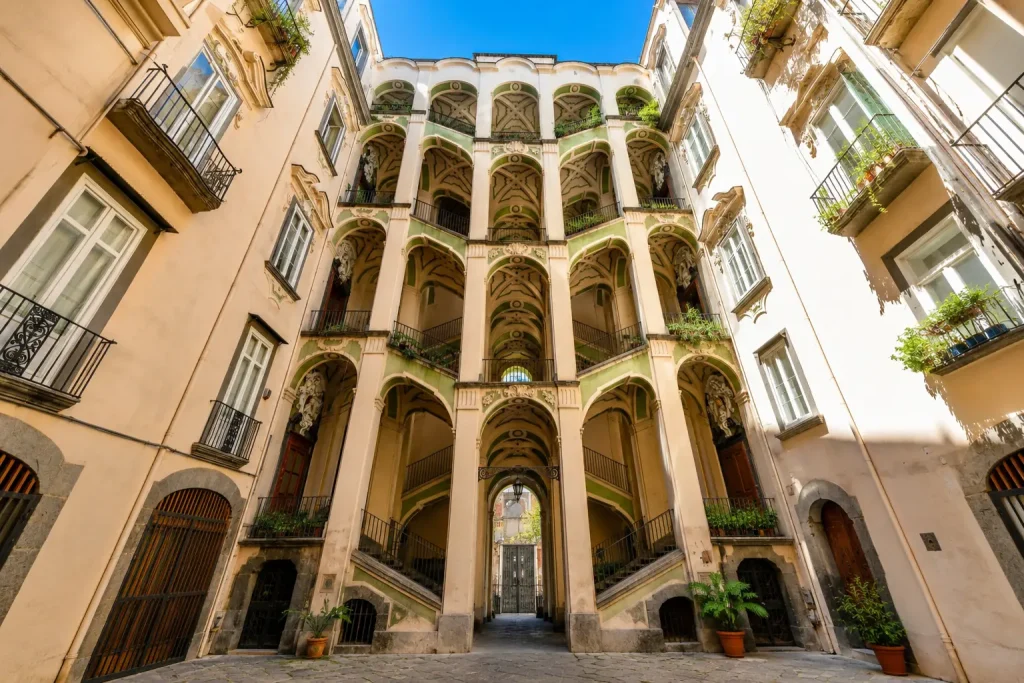 Palazzo dello Spagnolo courtyard in Naples featuring elegant Baroque staircases, arched galleries, and sunlit historic architecture in the Rione Sanità district.