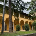 Historic courtyard of Biblioteca delle Oblate in Florence surrounded by arches, trees, and peaceful greenery under cloudy skies