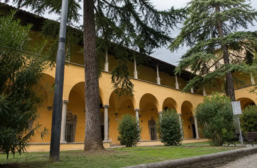 Historic courtyard of Biblioteca delle Oblate in Florence surrounded by arches, trees, and peaceful greenery under cloudy skies
