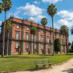 Capodimonte Museum in Naples surrounded by palm trees and gardens under a sunny sky with soft clouds.