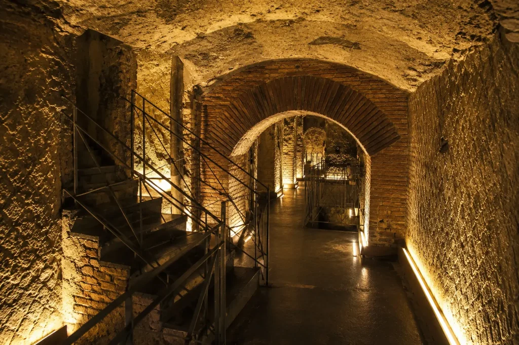 Ancient underground tunnels of Napoli Sotterranea featuring brick arches, volcanic stone walls, staircases, and warm atmospheric lighting beneath Naples, Italy.