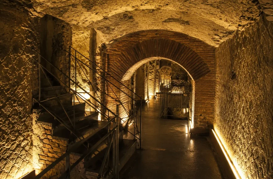 Ancient underground tunnels of Napoli Sotterranea featuring brick arches, volcanic stone walls, staircases, and warm atmospheric lighting beneath Naples, Italy.