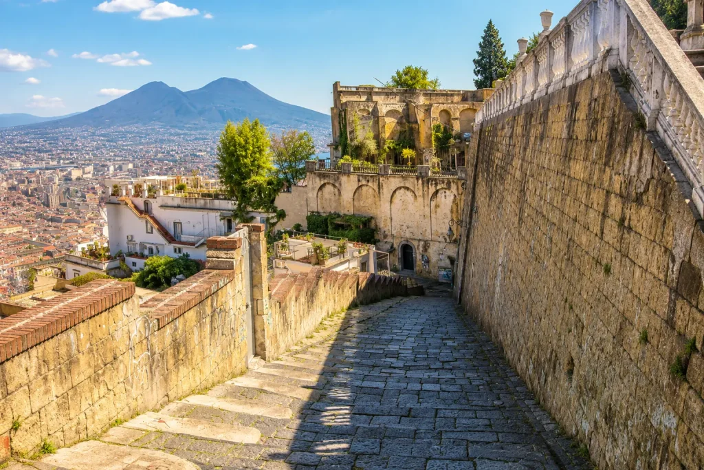 Historic stone staircase of Pedamentina a San Martino in Naples with panoramic city views and Mount Vesuvius under a sunny blue sky.