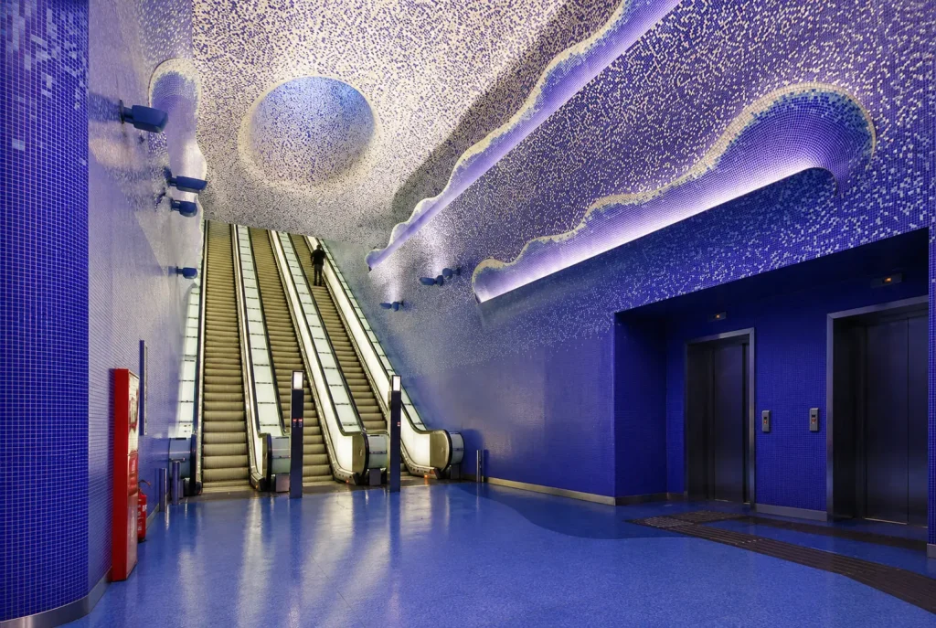 Futuristic blue interior of Toledo Metro Station in Naples with illuminated mosaic ceiling, escalators, and modern underground architecture.