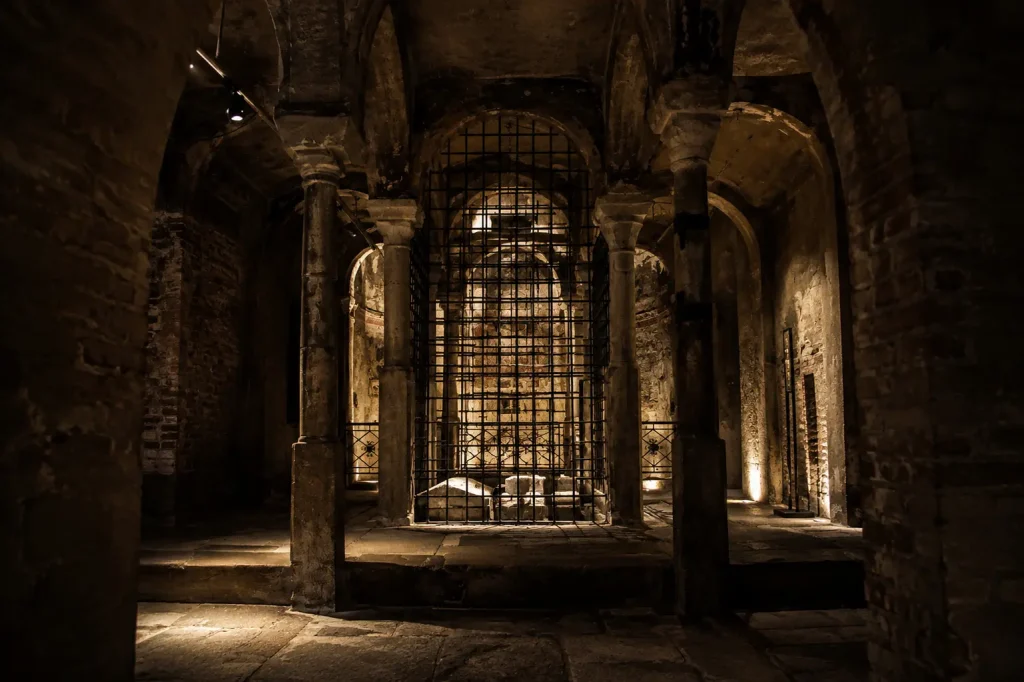 Atmospheric interior of the Crypt of San Sepolcro in Milan featuring ancient stone columns, medieval arches, and mysterious underground chambers