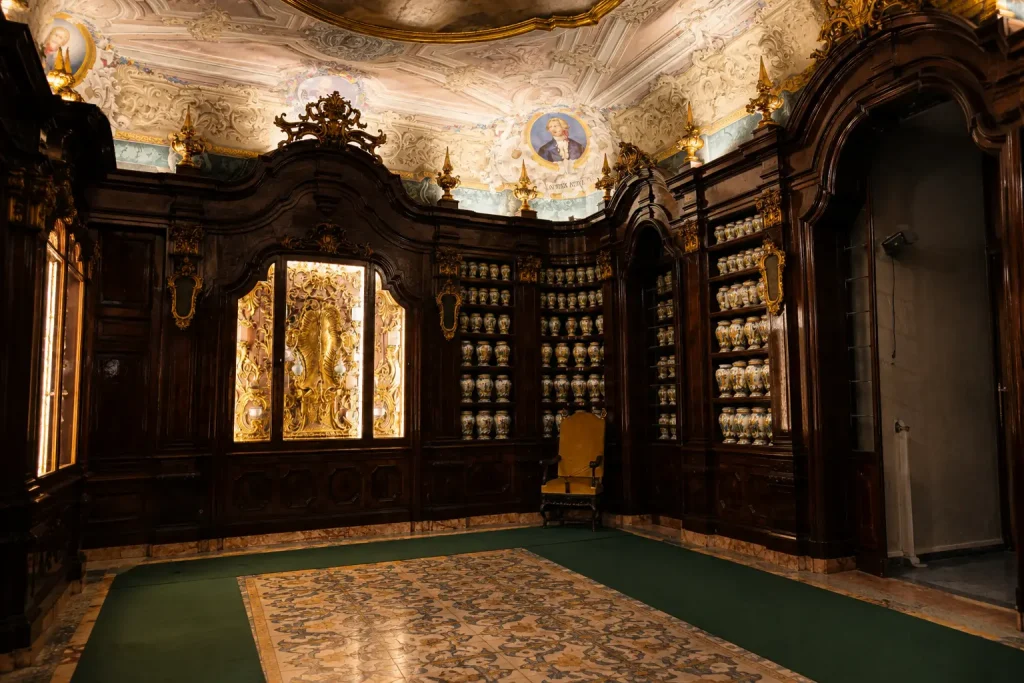 Historic majolica albarelli jars displayed in ornate walnut cabinets inside the Incurabili Pharmacy in Naples, one of Europe's finest surviving Baroque apothecaries.