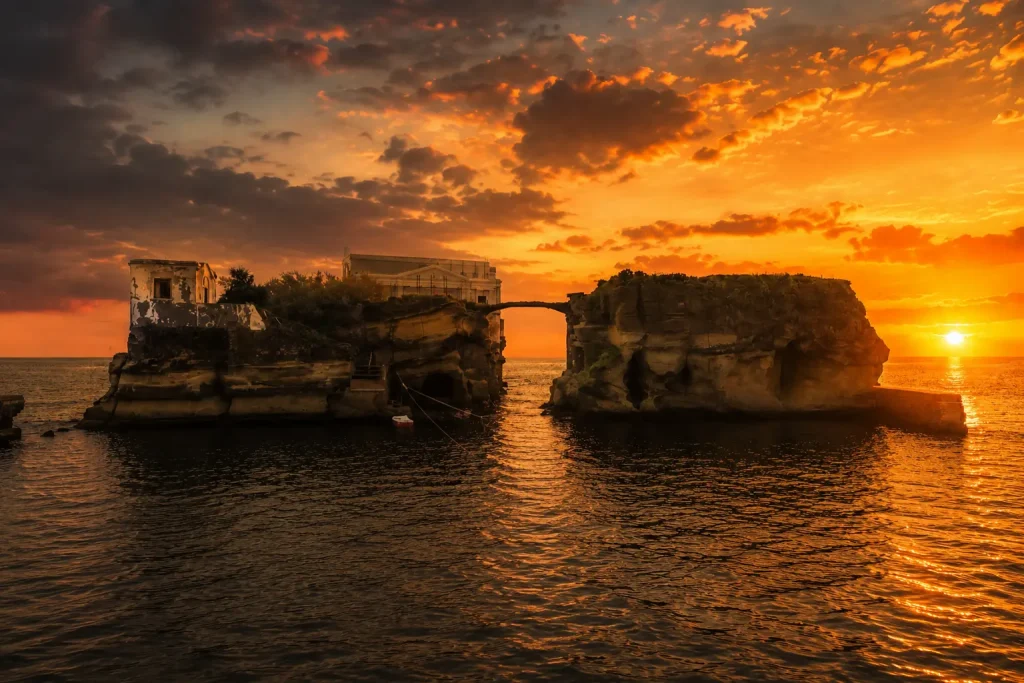 La Gaiola Island at sunset in Naples with glowing sky, historic bridge, and abandoned villa above the Mediterranean Sea