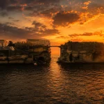 La Gaiola Island at sunset in Naples with glowing sky, historic bridge, and abandoned villa above the Mediterranean Sea