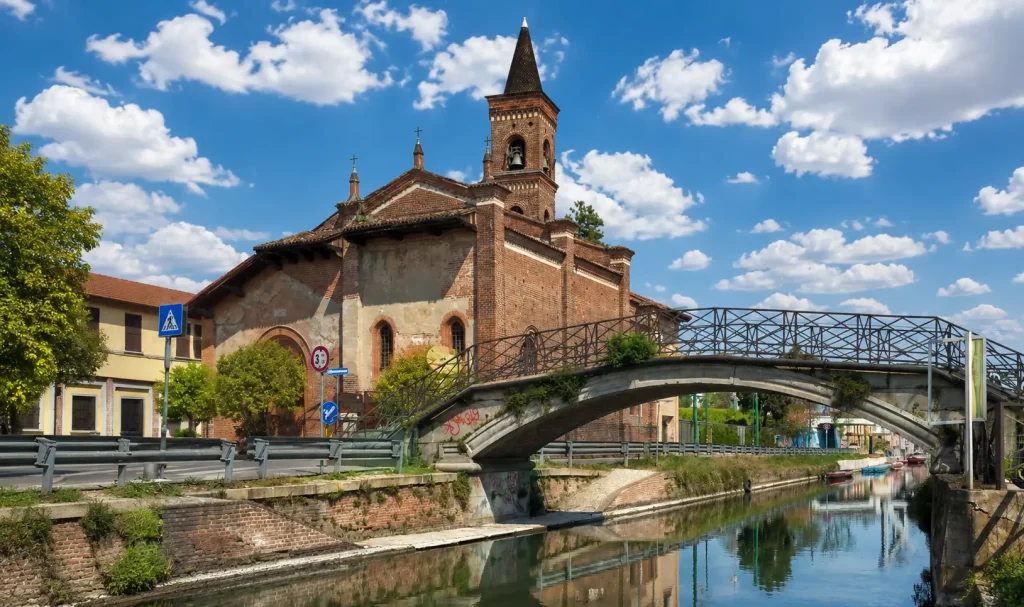 San Cristoforo sul Naviglio church and historic canal bridge in Milan under a bright blue sky with scattered clouds