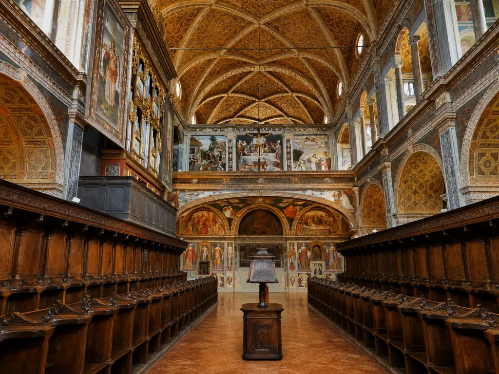 Interior of San Maurizio al Monastero Maggiore in Milan featuring Renaissance frescoes, ornate vaulted ceilings, and historic wooden choir stalls