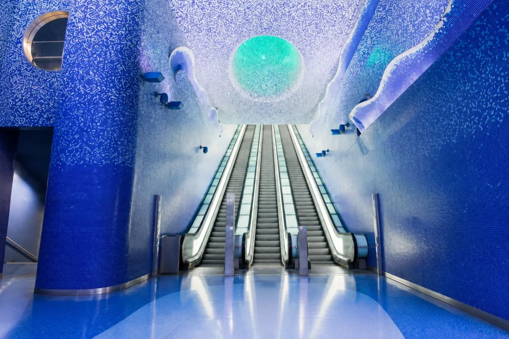 Empty blue mosaic escalator hall inside Toledo Metro Station in Naples, featuring the station's famous underwater-inspired architecture and contemporary art design.